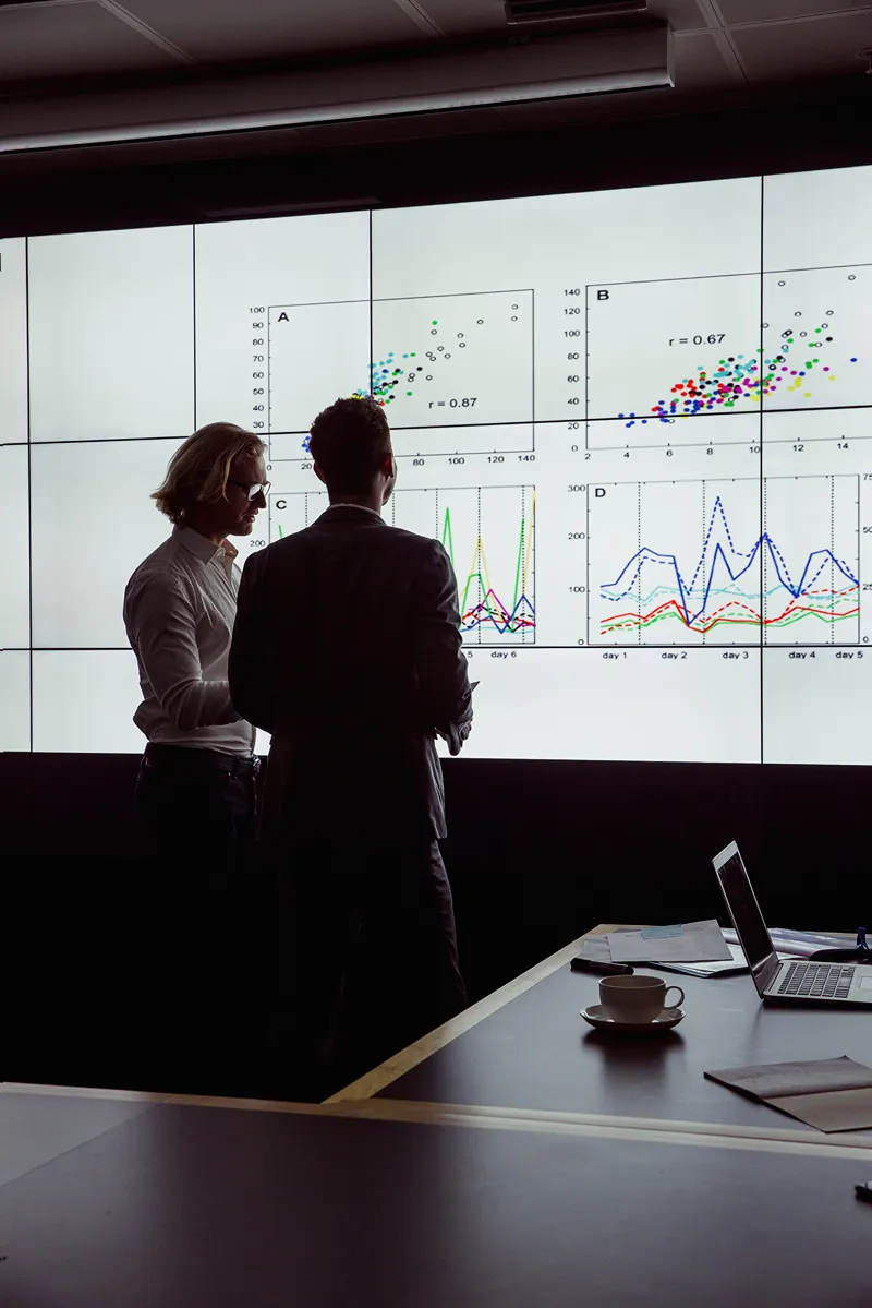 2 men looking at a screen showing data charts